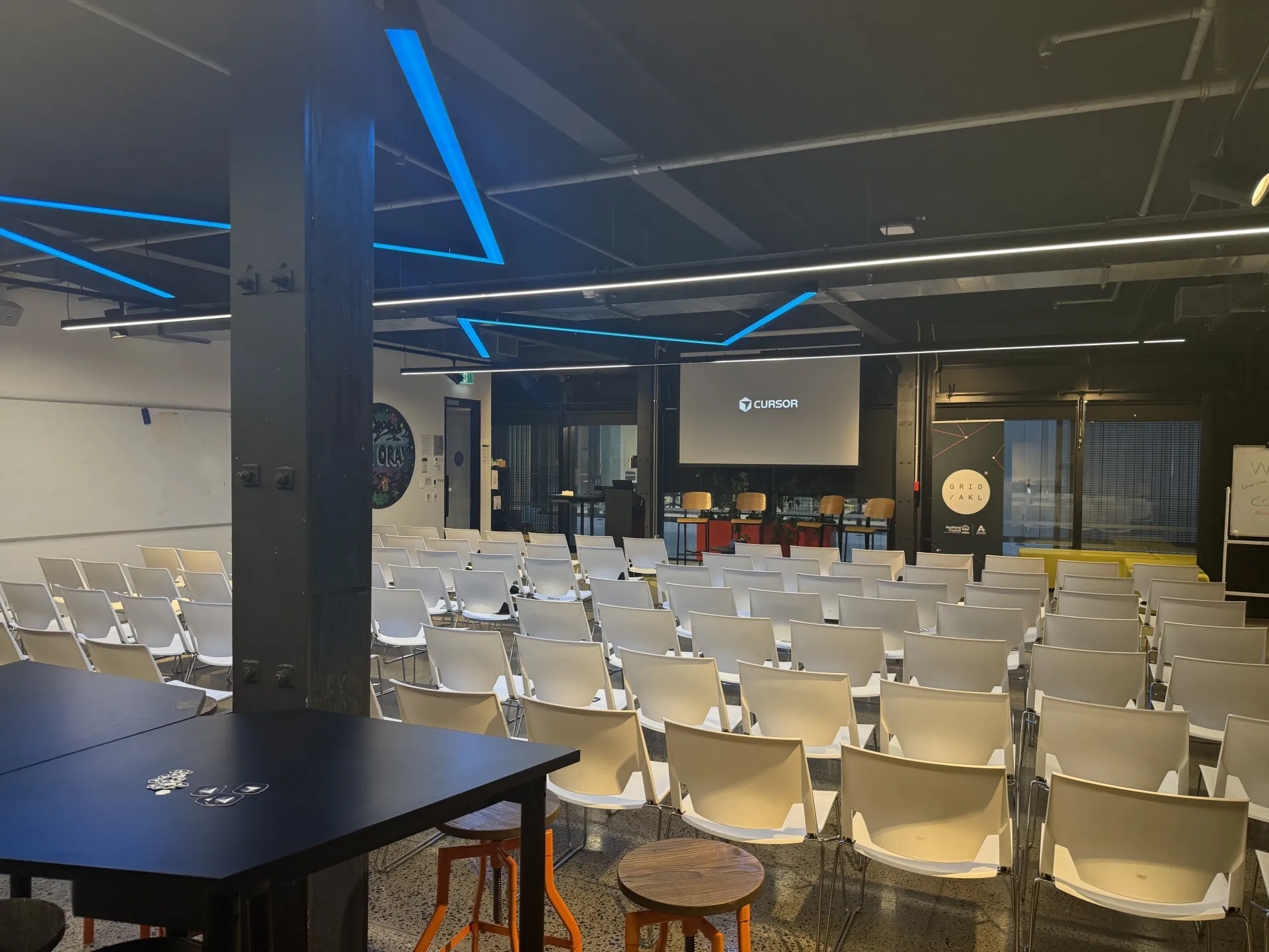 Event space at GridAKL with Cursor on screen and white chairs set for the meetup